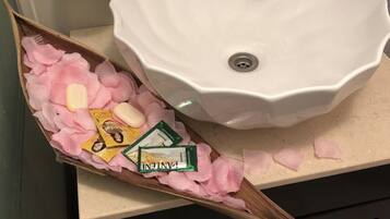 A bathroom with a white sink, a wooden decorative piece with pink petals and toiletries, and a glass soap dish.
