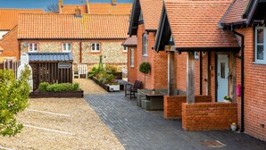 A courtyard with a gravel path, a seating area with chairs and a table, and a brick building with a door and windows. - Little Regent Hall (Sheringham)
