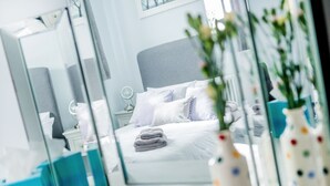 A modern bedroom with a neatly made bed, a bedside table, and a large mirror reflecting the room. - Little Regent Hall (Sheringham)