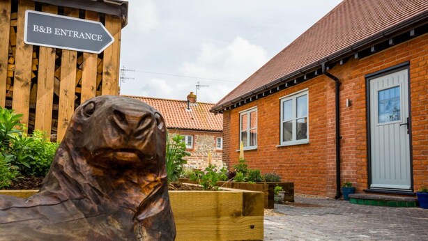 A wooden sculpture of a seal in front of a brick building with a sign reading "B&B ENTRANCE". - Little Regent Hall (Sheringham)