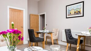A dining area with a table set for four, two chairs, a vase with flowers, and a framed picture on the wall. - Little Regent Hall (Sheringham)