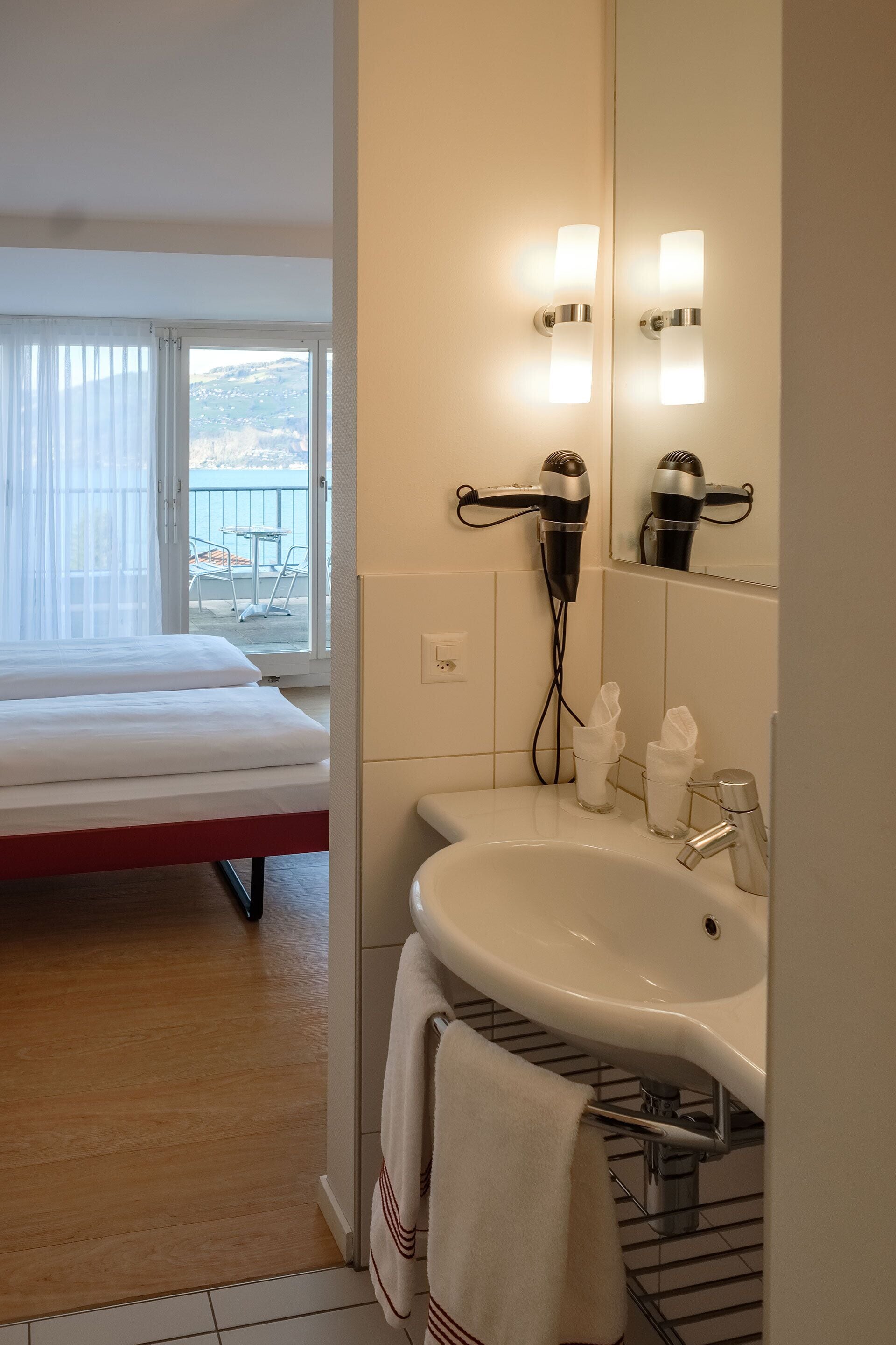 Une chambre d’hôtel avec un lit, une salle de bain comprenant un lavabo et un miroir, et une vue sur l’extérieur par une fenêtre.