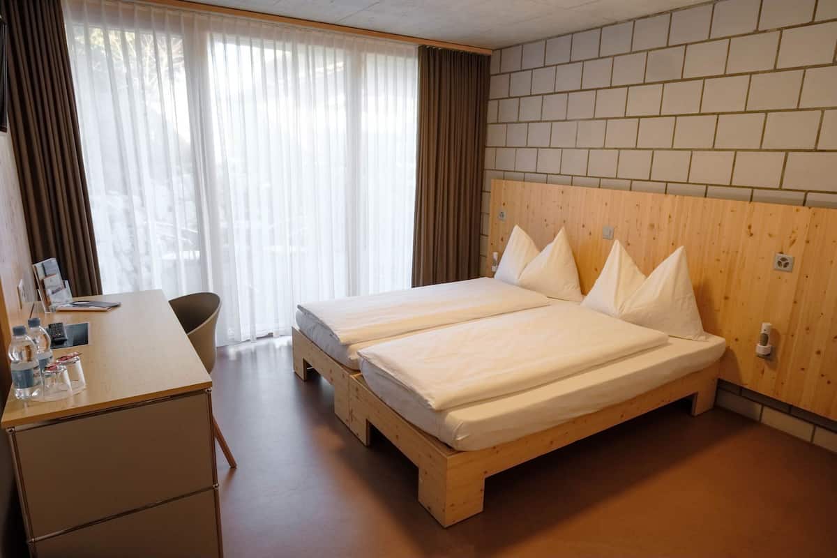 A hotel room with a wooden bed, a desk with a chair, and a window with curtains.
