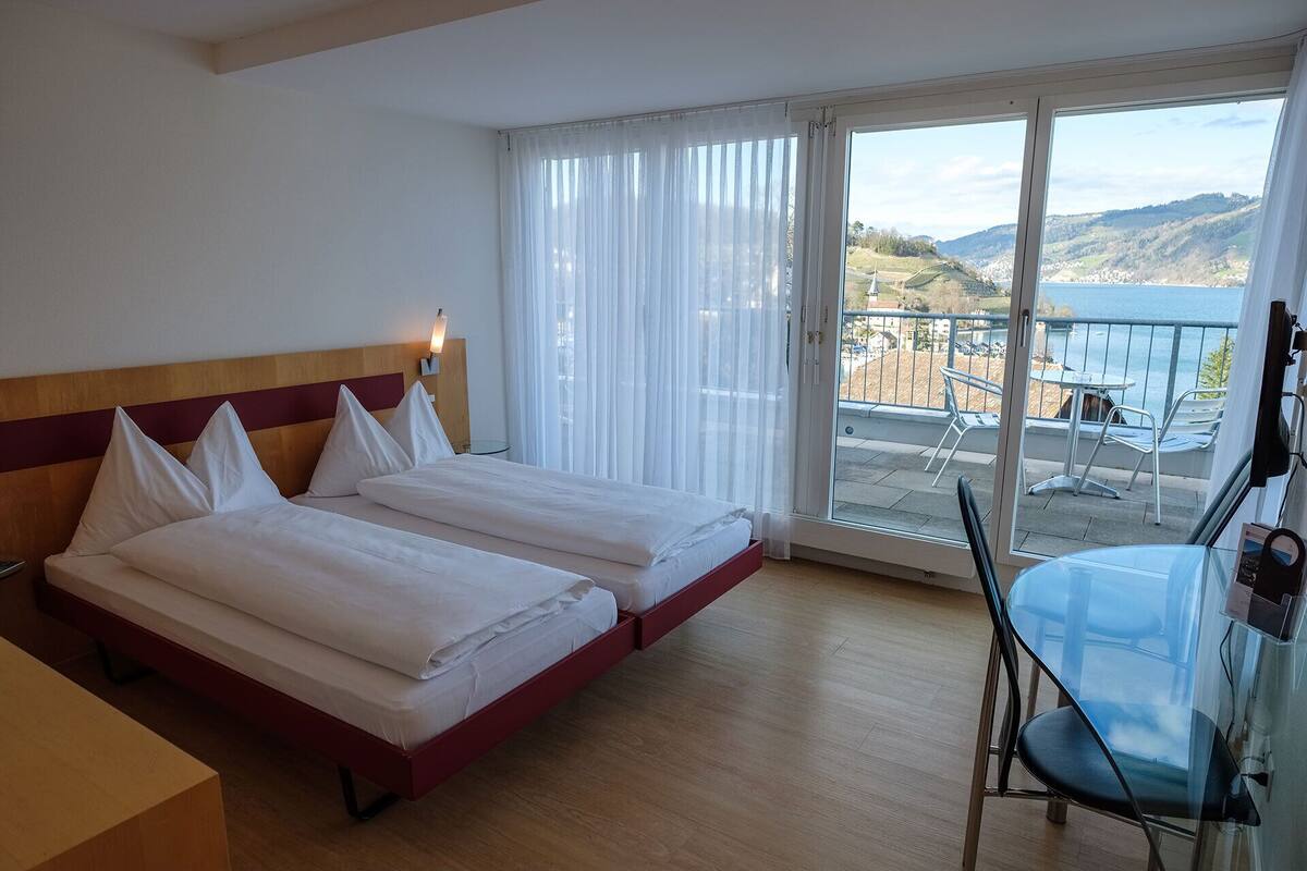A hotel room with two beds, a balcony with a table and chairs, and a view of the sea and hills.