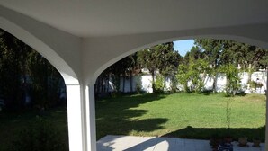 A covered patio area with a view of a grassy yard and a white wall in the background.