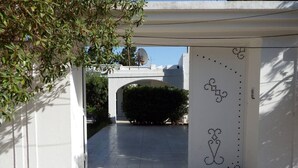 An entrance with a white door featuring a dotted design, leading to a paved pathway and a building in the background.