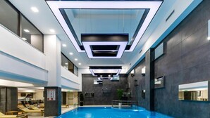 Una piscina interior moderna con agua cristalina, techo con iluminación empotrada y zona de descanso con tumbonas.