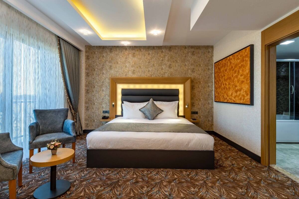 Hotellihuone, jossa on suuri sänky, tuoli, pieni pöytä ja suihkutila.
