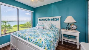 Un dormitorio con cama, mesita de noche, ventilador de techo y vistas al exterior.
