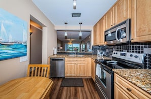 A modern kitchen with wooden cabinets, granite countertops, stainless steel appliances, and a dining area with a wooden table and chairs.