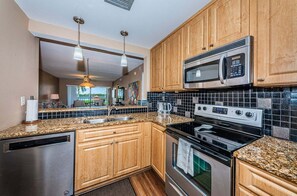 A kitchen with granite countertops, wooden cabinets, stainless steel appliances, and a view to the outside.
