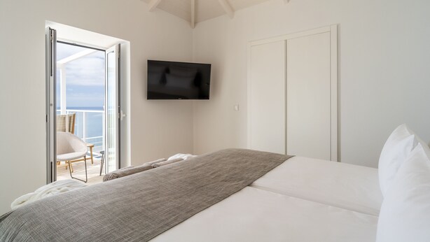 Un dormitorio con una cama, un televisor montado en la pared y un ventanal corredero que da a un balcón.
