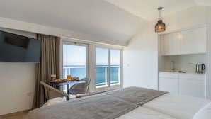 A hotel room with a bed, a TV, a dining table with chairs, a view of the sea, and a kitchenette. - Escarpa - the Madeira Hideaway (Ponta do Sol)