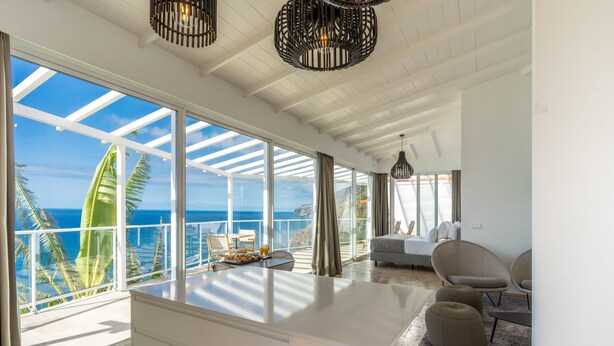 A spacious room with a large window overlooking the ocean, a white ceiling, and a modern chandelier. - Escarpa - the Madeira Hideaway (Ponta do Sol)