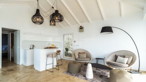 A modern living space with a kitchen area, two seating areas with ottomans, and a large window providing natural light. - Escarpa - the Madeira Hideaway (Ponta do Sol)