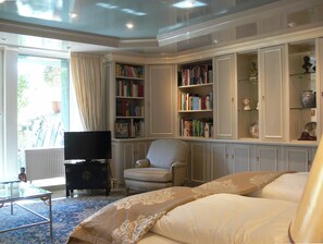 A living room with a sofa, armchair, television, and bookshelves. - Die Villa Mettmann (Mettmann)
