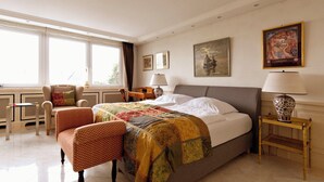 A hotel room with a large bed, two chairs, a desk, and a window with curtains. - Die Villa Mettmann (Mettmann)