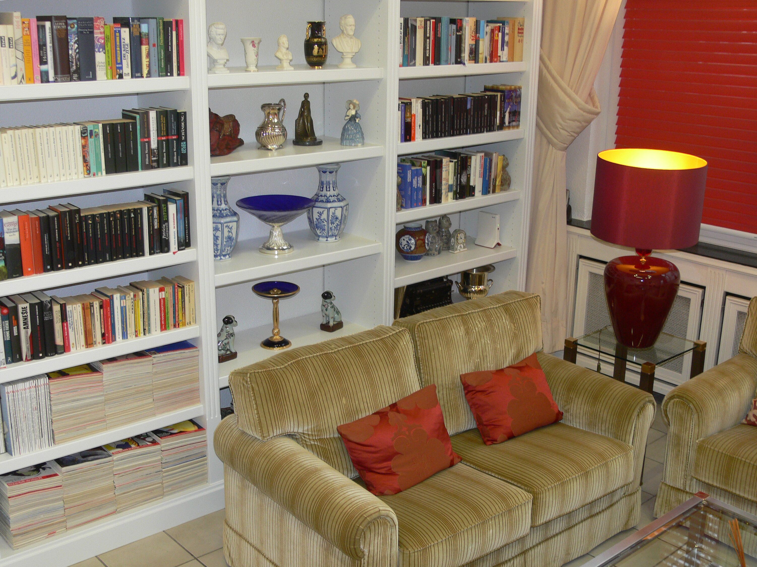 Een woonkamer met een bank, boekenkasten, decoratieve objecten en een lamp.