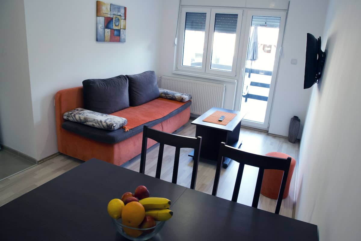 A modern living room with a sofa, a dining table with chairs, and a fruit bowl.