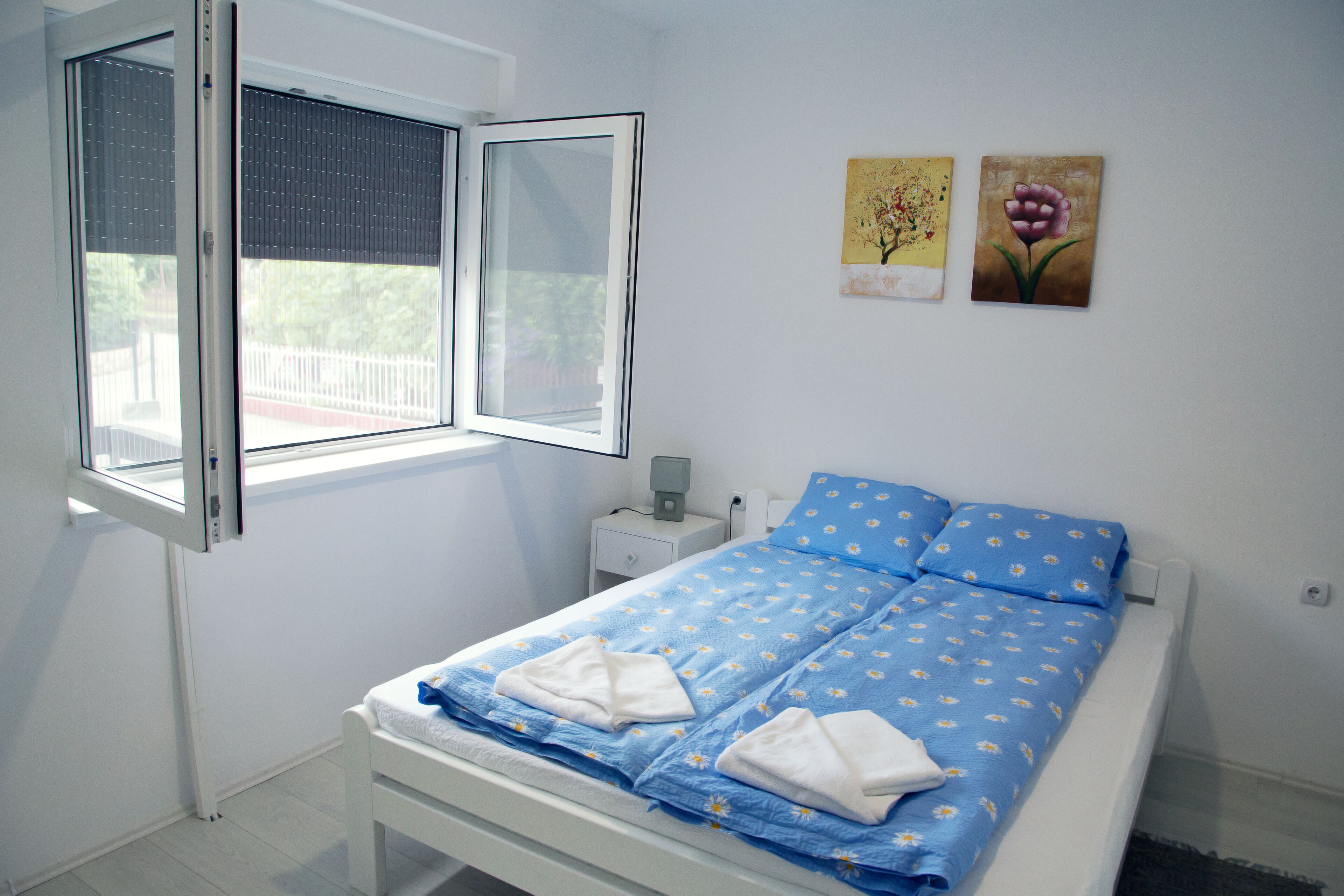 Een slaapkamer met een bed, een raam, een nachtkastje en twee decoratieve wandpanelen.