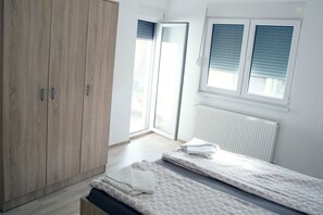 A bedroom with a wooden wardrobe, a window with blinds, and a radiator. - Apartments Velickovic (Soko Banja)