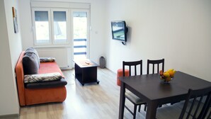 A compact living space with a sofa, a small table, a TV, and a dining table with chairs. - Apartments Velickovic (Soko Banja)