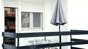 A balcony with a black railing, a white window with blinds, and a grey umbrella. - Apartments Velickovic (Soko Banja)