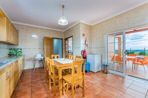 A kitchen with wooden cabinets, a dining table with chairs, a blue trash bin, and a fire extinguisher. - Villa da Horta, a beautiful extensive villa in a peaceful location (Alcantarilha)