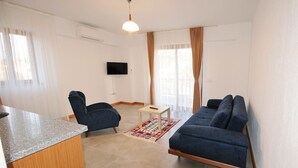 A modern living room with a TV, two sofas, a small table, and a kitchen area with a granite countertop. - Karaincir Suit Otel (Datça)