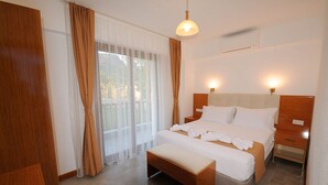 A hotel room with a large bed, a bench, a bedside table, a nightstand, and a window with curtains. - Karaincir Suit Otel (Datça)