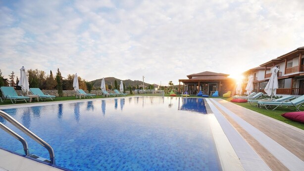 A swimming pool with lounge chairs and umbrellas, surrounded by a building with a patio area. - Karaincir Suit Otel (Datça)