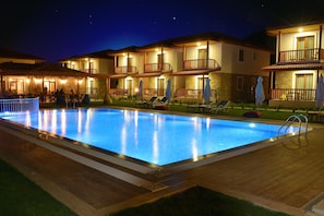 Una piscina con sillones de descanso y sombrillas, rodeada de edificios de varios pisos con balcones y terrazas.