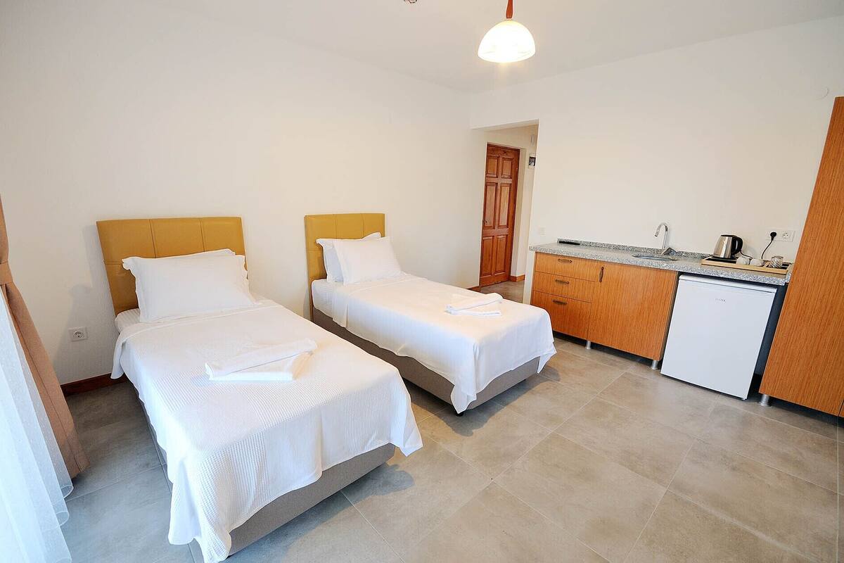 Une chambre d’hôtel avec deux lits simples, une kitchenette et une porte en bois.