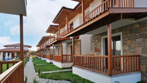 A row of modern bungalows with wooden balconies, a paved walkway, and a well-maintained lawn. - Karaincir Suit Otel (Datça)