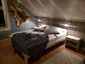 Una camera da letto con un letto, un comodino, una testiera in legno, un tappeto di pelliccia e un cappotto di pelliccia appeso al muro.