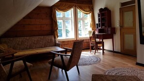 A cozy attic room with a wooden ceiling, a sofa, a dining table, and a wooden cabinet. - Rødseter Inn (Sogndal)