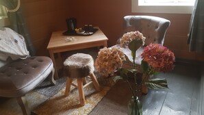 A cozy room with a wooden floor, a cushioned bench, a small stool, a wooden table with a tray of items, and a chair with a cushion. - Rødseter Inn (Sogndal)