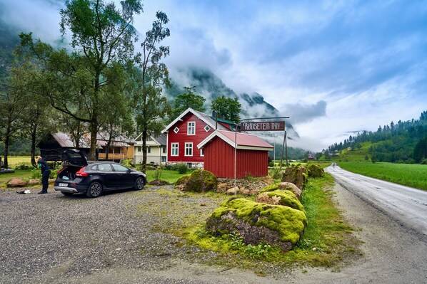 A red building with a sign reading "Rødseter Inn" in a rural setting with a gravel road and greenery.