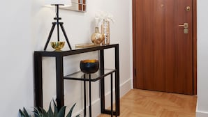 A hallway with a wooden door, a console table with decorative items, a floor lamp, and a potted plant. - Lux Central Apartment At Kolonaki (Athens)