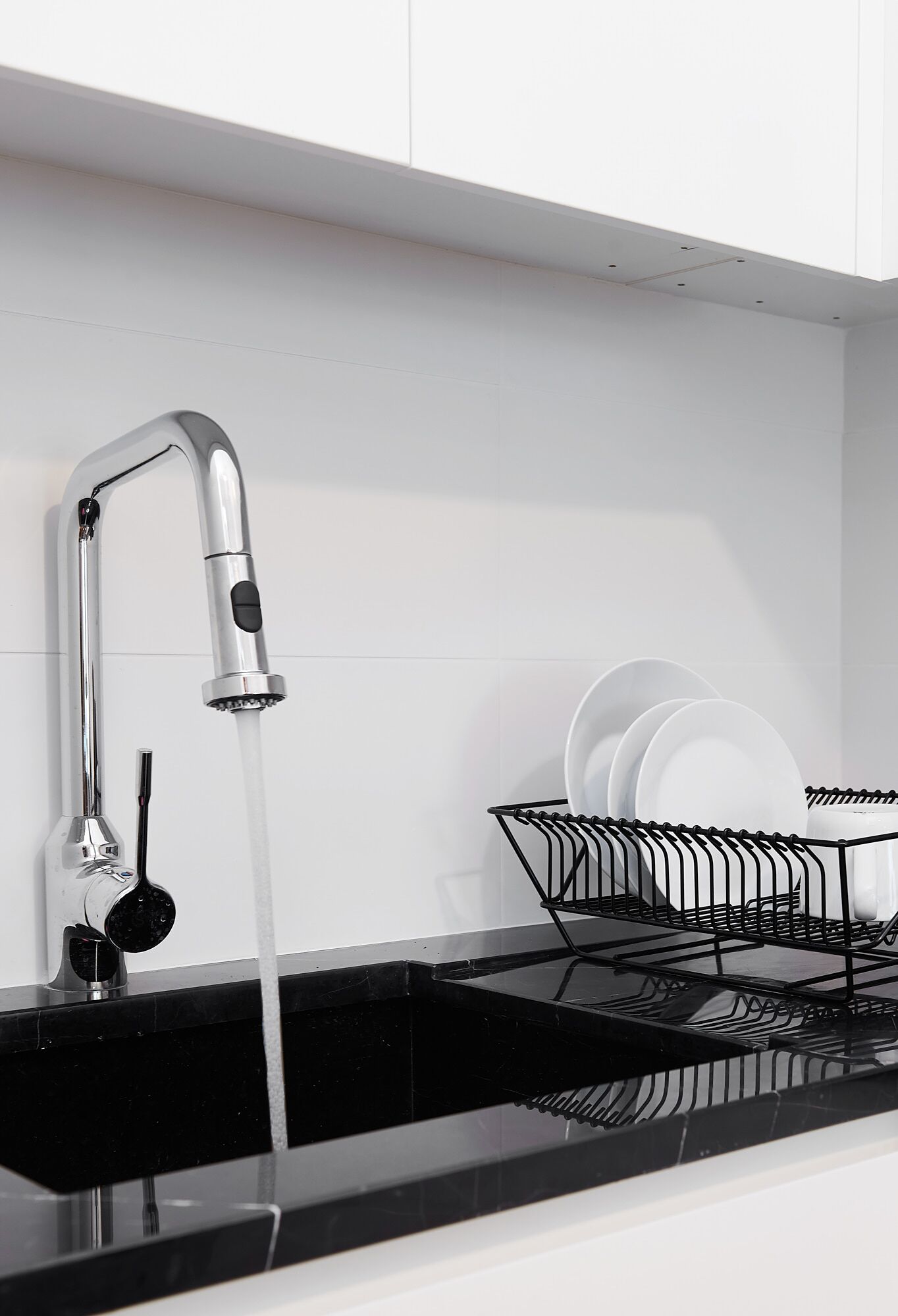 A modern kitchen with a stainless steel faucet, a black countertop, and a dish rack with white plates.