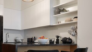 A modern kitchen with white cabinetry, a black island, and two black chairs. - Lux Central Apartment At Kolonaki (Athens)