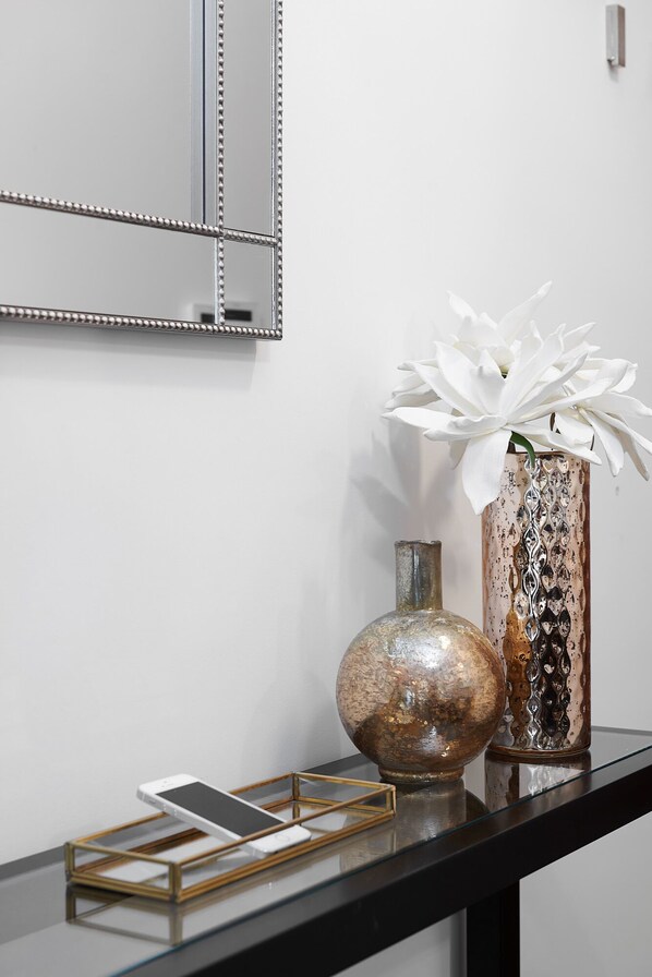 A black console table with a smartphone, a round vase, and a tall vase with white flowers.