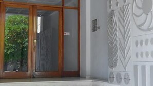 A building entrance with a wooden ceiling, a glass door, and a set of stairs leading up to a white wall with decorative panels. - Lux Central Apartment At Kolonaki (Athens)