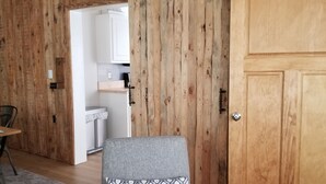 Een kamer met een houten wand, een bed met gestreepte kussens, een tafeltje en een deur.