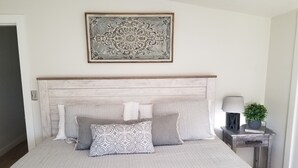 Een slaapkamer met een houten hoofdbord, een bed met een decoratief sprei en een nachtkastje met een lamp en een kleine plant.