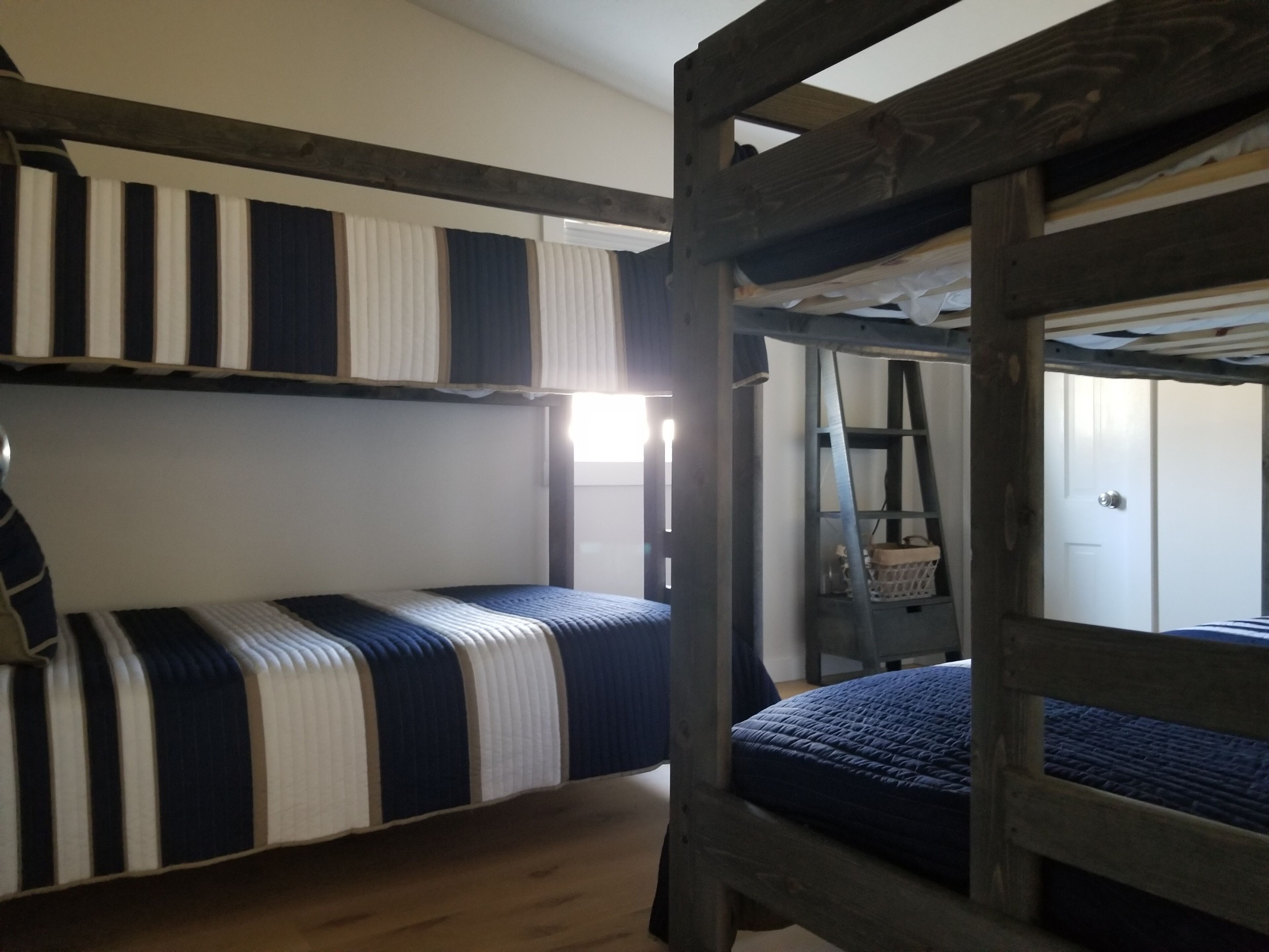 Een slaapkamer met een stapelbed, gestreepte beddengoed, een ladder en een deur op de achtergrond.