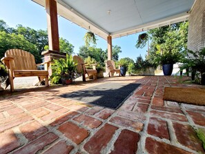 A covered patio area with brick flooring, wooden Adirondack chairs, and potted plants. - Charming, Renovated Historic Country Store; close to Athens and the Broad River (Danielsville)