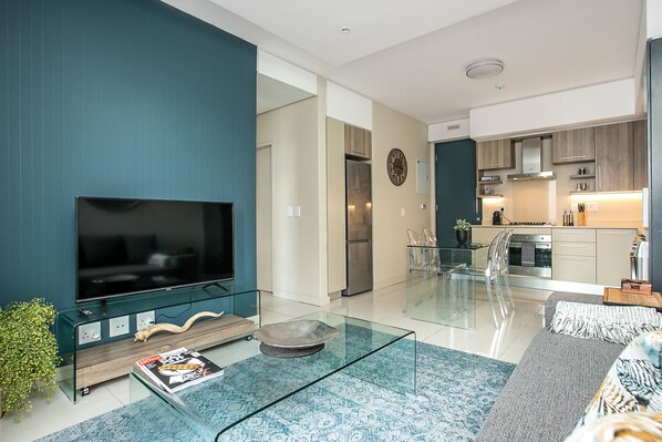 A modern living room with a flat-screen TV, glass coffee table, and a sofa. - 801 The Tyrwhitt Rosebank - Adults Only (Johannesburg)