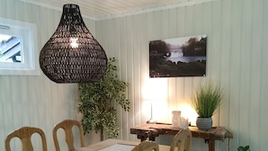 A dining area with a wooden table, chairs, a hanging light fixture, a potted plant, and a framed picture on the wall.