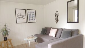 A living room with a grey sofa, a small round table, a potted plant, and two framed artworks on the wall.